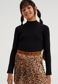 Melna ribota krekla ar garām piedurknēm apģērbs, kas savienots ar griezuma svārkiem, kuru josta ir oranžā krāsā ar uzrakstu "EASY THERE" un brūnas un melnas krāsas leopardu rakstu.