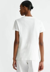 T-shirt bianco a maniche corte realizzato in materiale morbido, con scollo rotondo e vestibilità rilassata, con orlo posteriore leggermente più lungo.