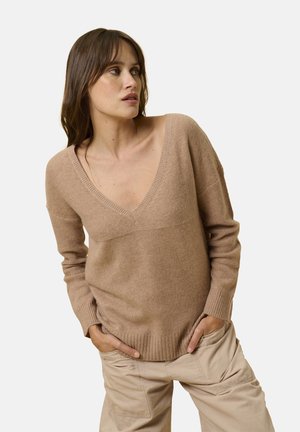 Beige gebreide trui met een diepe V-hals, geribbelde manchetten en zoom. Zachte textuur, comfortabele pasvorm, gecombineerd met lichtgekleurde cargobroeken.