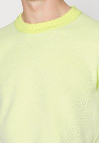 Pull-over jaune clair avec un motif tricoté texturé, col rond côtelé et manches courtes. Tissu lisse avec une apparence respirante.