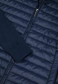 Tumši zila jaciņa ar centrālu rāvējslēdzēju un piedurkni no ribota trikotāžas auduma.