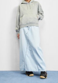 Sudadera gris con bolsillo tipo canguro, combinada con una falda larga de mezclilla azul clara. Zapatos negros con suelas de goma parcialmente visibles en la parte inferior.