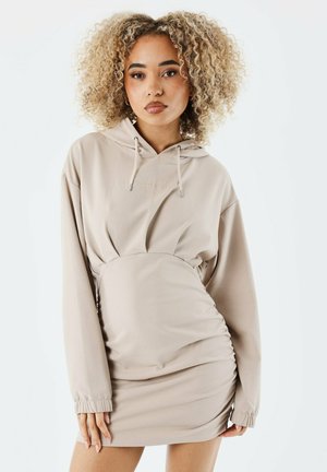 Beige hoodie jurk met lange mouwen, elastische zoom en capuchon met trekkoord. Gladde textuur, aansluitende silhoët en geplooide taille details.