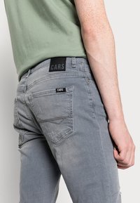 Grijze denim jeans met een slim fit, met een zwarte merkband in de taille, achterzakstiksel details en subtiele vervaagde accenten.
