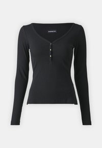 Musta pitkähihainen yläosa, joka on valmistettu ribbineuloksesta, jossa on V-kaula-aukko, kolme kultasävyistä nappia rintamuksessa ja vartalonmyötäinen siluetti.