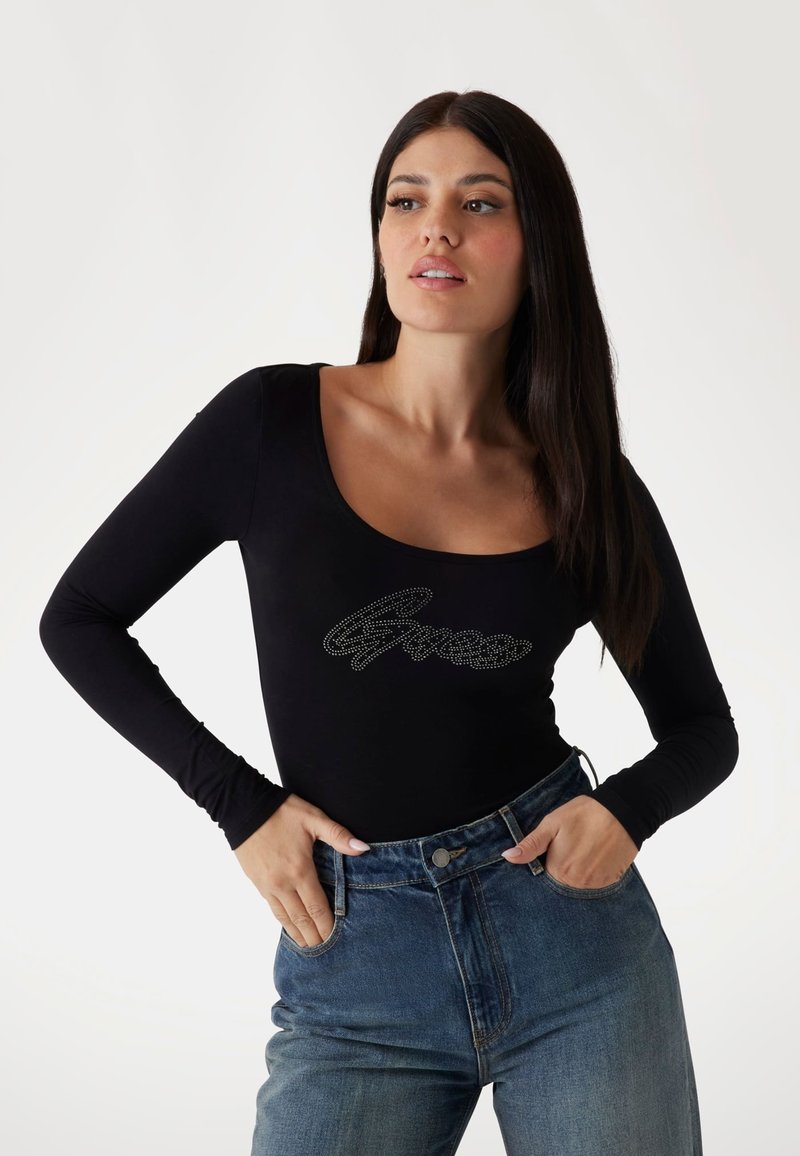 Black long-sleeve bodysuit featuring a scoop neckline and a rhinestone-embellished logo on the front, paired with high-waisted blue jeans.