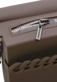 Brązowa torba silikonowa o teksturowanej powierzchni, z zamkiem błyskawicznym i wyraźnym detalem w postaci łańcucha po boku. Posiada małą metkę z logo.