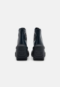 Bottines noires texturées avec une finition brillante, arborant un patch en forme de logo rond et une semelle épaisse à motifs pour une meilleure traction.