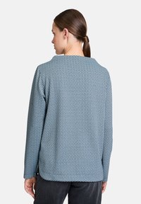 Blau gemusterte Jacke mit weicher Textur, bietet einen runden Ausschnitt und lange Ärmel, die ein sich wiederholendes hexagonales Design zeigen.