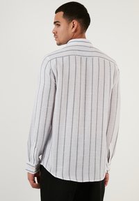 Camicia bianca a maniche lunghe con righe verticali blu navy, con colletto a bottoni e bottoni ai polsini. Tessuto morbido e testurizzato.