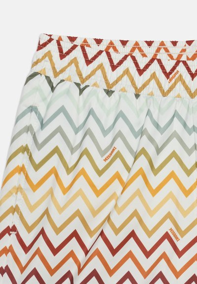 Gros plan sur un tissu avec un motif zigzag multicolore dans des tons de vert, jaune, orange et rouge, avec le logo texte "MISSONI".