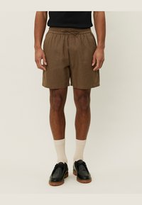 Pantalones cortos de lino marrón con cinturilla elástica y cordón. Llevados con calcetines de canalé color crema y zapatos de cuero negro.