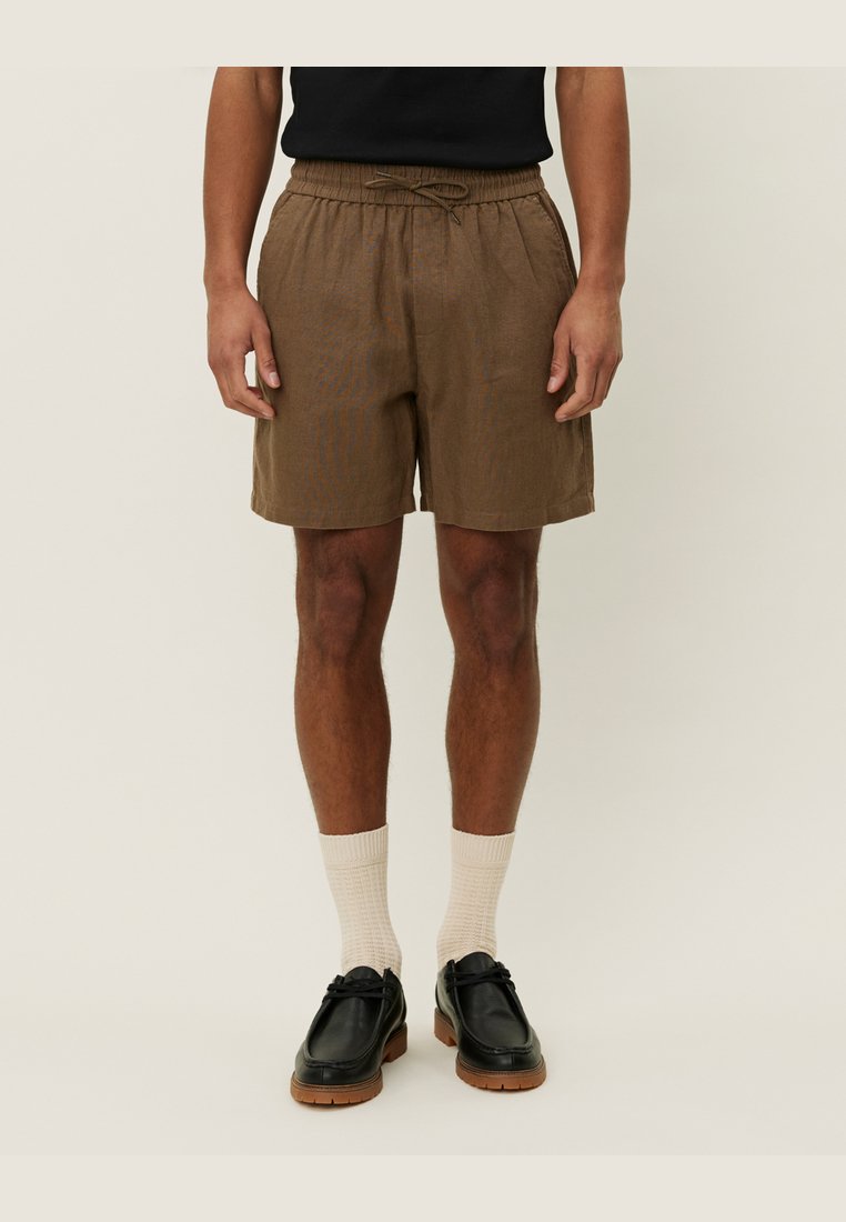 Pantalones cortos de lino marrón con cinturilla elástica y cordón. Llevados con calcetines de canalé color crema y zapatos de cuero negro.