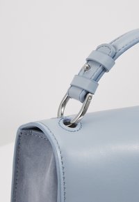 Sac à main en cuir bleu clair avec un design structuré, doté d'une boucle en métal argenté et d'un détail de bordure cousue.