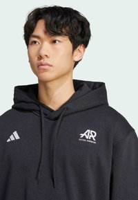 Crna dukserica od pamučnog materijala s dodatkom sintetike, s prednjim džepom, kapuljačom na vezanje i bijelim Adidas Runners logotipom na prsima i lijevom ramenu.