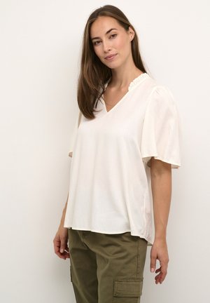 Bluză albă, cu mâneci scurte, cu decolteu în V și detalii cu volane la gât. Material moale, ușor, cu un ușor luciu. Asortată cu pantaloni de culoare verde măslin.