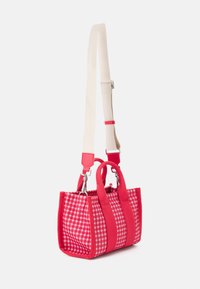 Sac rouge à carreaux avec un tissu texturé, des poignées solides rouges contrastantes et une bandoulière beige amovible. Forme compacte et rectangulaire.