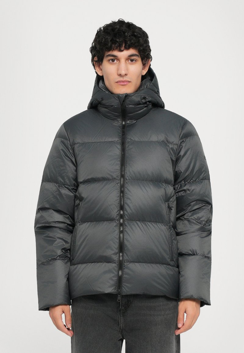 Graue Daunenjacke mit Kapuze, die über ein gestepptes Design, einen Frontreißverschluss und eine leicht glänzende Textur verfügt. Getragen über dunkelgrauen Hosen.