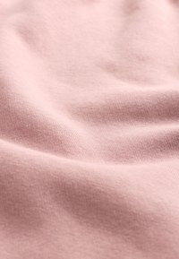 Ljust rosa tyg med en slät yta och lätt fall. Väven är tät, vilket visar subtila variationer i nyans över ytan.
