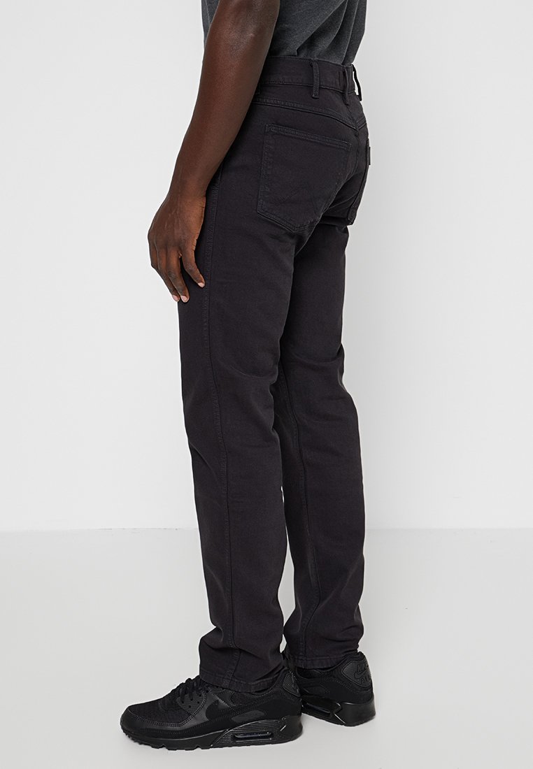 Czarne dżinsy o dopasowanym kroju, z tylnymi kieszeniami i gładką fakturą. Noszone z czarnymi butami sportowymi.