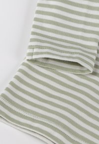 Gestreifter Stoff mit abwechselnden hellgrünen und weißen Linien, weicher Textur und gesäumten Kanten. Nahaufnahme des Materials.