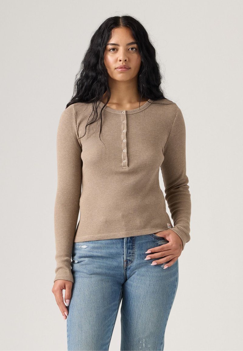 Top de canalé beige de manga larga con cuello redondo y botón frontal, combinado con vaqueros desgastados de color azul claro.