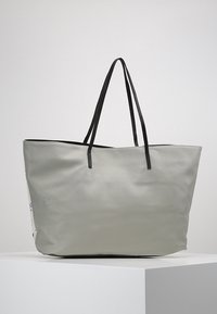 Sac cabas gris à finition texturée, avec des poignées doubles noires et une ouverture supérieure. Présente un design minimaliste sans éléments métalliques visibles ni motifs.