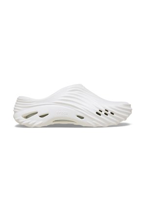 White slip-on footwear with a wavy design, made from lightweight material. Features ventilation holes and a smooth, rounded shape.