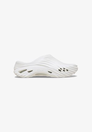 White slip-on footwear with a wavy design, made from lightweight material. Features ventilation holes and a smooth, rounded shape.