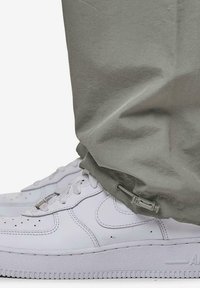 Grå bukser med snor i buksebenene, kombinert med hvite sneakers. Sneakersene har perforerte detaljer og teksturerte såler.