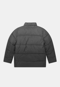 Chaqueta de abrigo negra con cuello alto, diseño acolchado horizontal y hombros caídos. Textura suave y mate con un corte relajado.