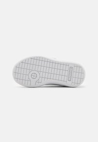 Suela de goma blanca con un patrón texturizado, que presenta un detalle circular y el nombre de la marca "LACOSTE" grabado cerca del talón.