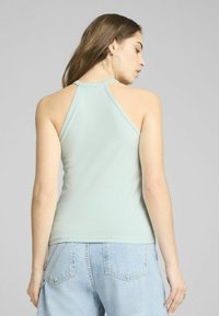 Lichtblauwe haltertop van gladde stof, met een aansluitend ontwerp en open rug. Gecombineerd met lichtgekleurde spijkerbroeken met hoge taille.