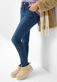 Blå denim skinny jeans med lomme detaljer, parret med lyse beige pelsforede ankelstøvler. Outfittet har et struktureret brunt yderstykke.