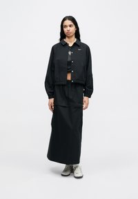 Μ αύρο κοντό μπουφάν με κούμπωμα κουμπιών και ελαστικές μανσέτες, σετ με μακρύ φούστα στο ίδιο ύφασμα. Και τα δύο φτιαγμένα από ελαφρύ ύφασμα.