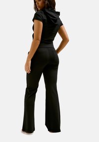 Zwart activewear set bestaande uit een T-shirt met korte mouwen en een capuchon, en flared broeken. Gladde textuur en aansluitend ontwerp, met achterzakken op de broeken.