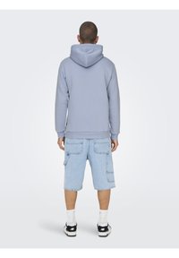 Sudadera gris con capucha ajustable, combinada con pantalones cortos cargo de color azul claro que cuentan con múltiples bolsillos. El conjunto se completa con zapatillas negras.