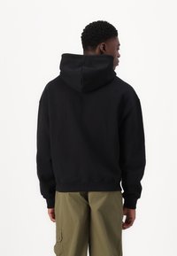 Svart hettegenser med avslappet passform, ribbede mansjetter og nederkant. Stoffet ser mykt ut med en glatt tekstur. Brukt sammen med olivengrønne cargo-bukser.