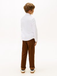 Biała koszula z długim rękawem, brązowe spodnie z sztruksu i białe sneakersy. Koszula ma kołnierzyk; spodnie są luźne i mają podwinięte mankiety.