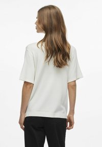 Top bianco a maniche corte con vestibilità comoda, dotato di scollo rotondo e texture liscia, abbinato a pantaloni neri dal design minimalista.