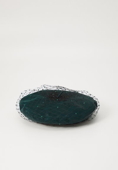 Teal ovaalne kangast aksessuaar, millel on tekstureeritud pind, kaetud musta võrguga ja dekoratiivsete aktsentidega, mille keskel on kaunistus.