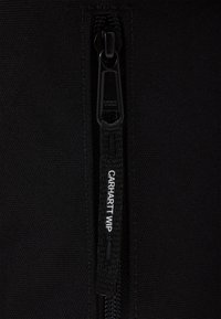 Veste zippée noire avec une fermeture éclair YKK dotée d'un tirette de marque « CARHARTT WIP ». Tissu texturé avec une finition lisse.