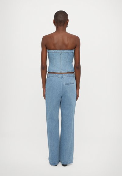 Denim stroppeløs topp med en tettsittende kropp, kombinert med vide lyseblå bukser. Stoffet har en glatt tekstur og minimal detailing.