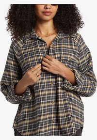 Sort, gul og hvid ternet flannel skjorte med knaplukning og brystlomme. Har optrukne ærmer og løs pasform.