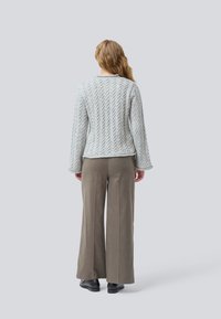 Maglione grigio chiaro a maglia con un motivo a treccia testurizzato e maniche svasate, abbinato a pantaloni beige a gamba larga e scarpe nere.