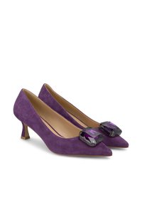 Scarpe col tacco alto in suede viola con punte affilate, caratterizzate da grandi accenti viola sfaccettati sulla parte anteriore e una zeppa corta e quadrata.