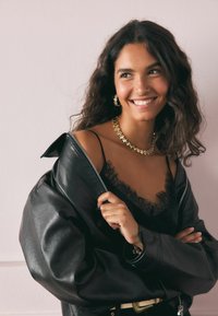 Must musta üleõlgadega jope, millel on lukku, kiht musta pitsilised kampsun. Kuldne tähekaelakee ja kõrvarõngad pakuvad metallilisi aktsente.