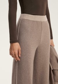 Pantaloni a gamba larga in morbido tessuto a maglia color nocciola chiaro con vita a coste. Cuciture laterali affusolate e finiture pulite.