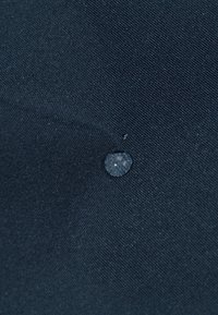 Dark blue fabric with a textured surface, featuring a round droplet of water on it. The material appears water-resistant.