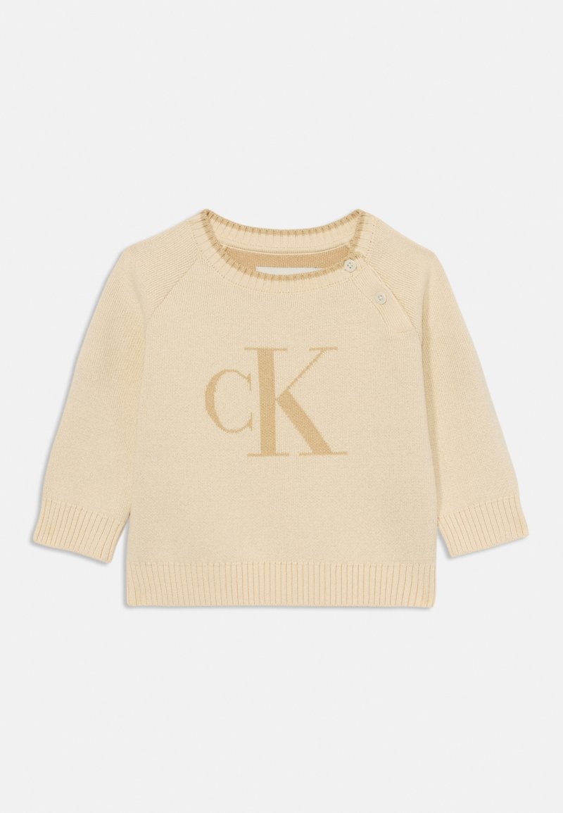 Sweater tricotado em tom de creme com decote redondo, mangas curtas e detalhes canelados. Apresenta um logo "CK" em bege claro na parte da frente.